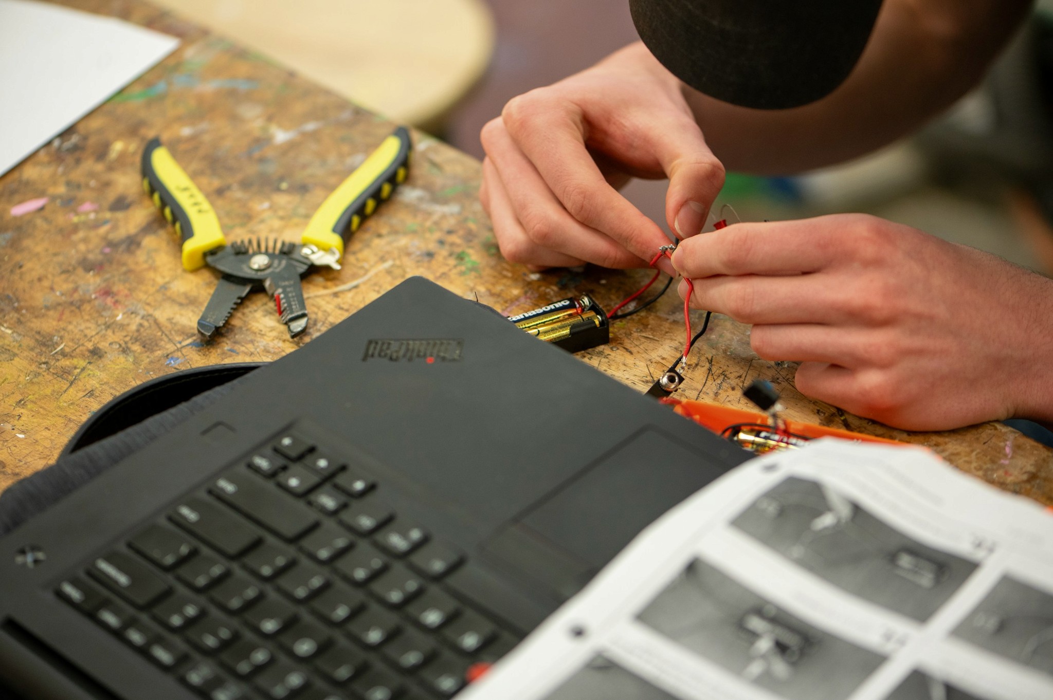 Hands wiring electronics next to a laptop